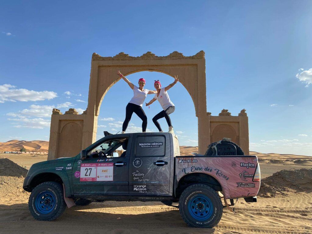 Dans le désert marocain, Angélina et Julie posent sur le toit de leur 4X4, heureuses de participer au Trophée Roses des Sables